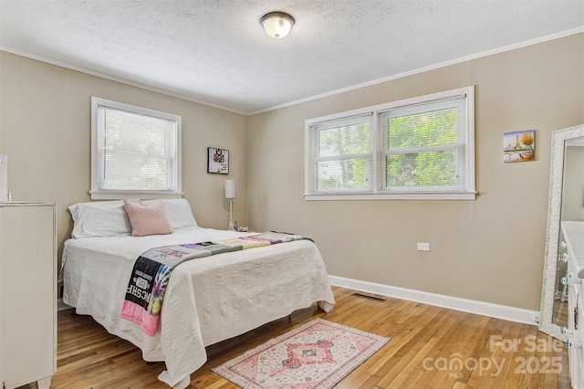bedroom with a textured ceiling, baseboards, ornamental molding, and wood finished floors
