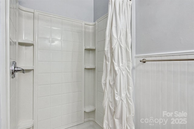 full bathroom with wainscoting and a tile shower