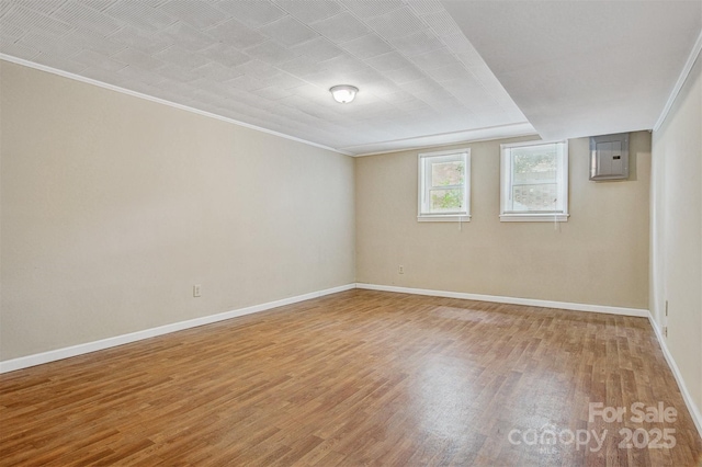 unfurnished room featuring crown molding, baseboards, electric panel, and light wood-type flooring