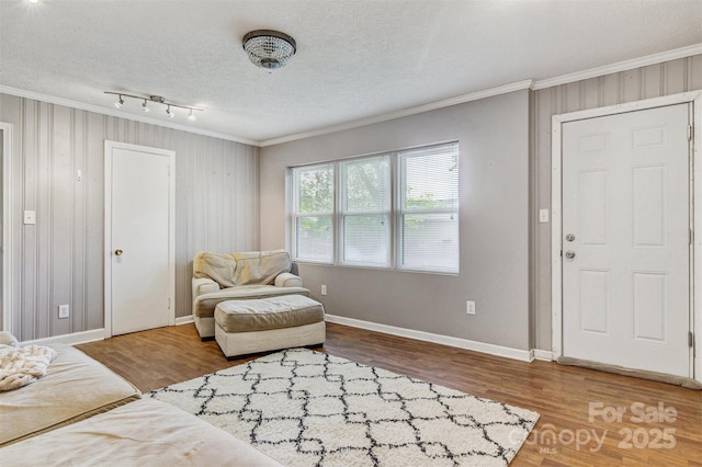 interior space with a textured ceiling, baseboards, ornamental molding, and wood finished floors