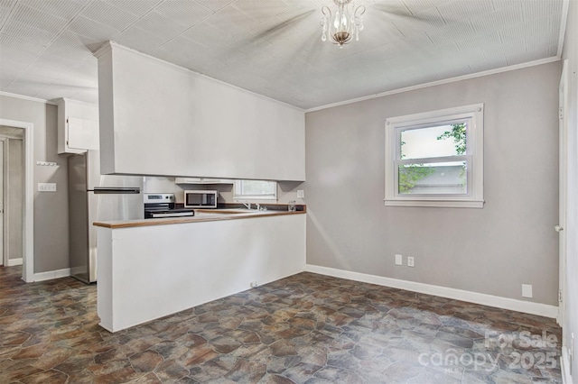 kitchen with stone finish floor, ornamental molding, stainless steel appliances, and white cabinetry
