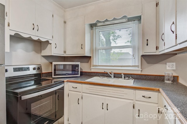 kitchen featuring dark countertops, a sink, ornamental molding, stainless steel appliances, and white cabinetry