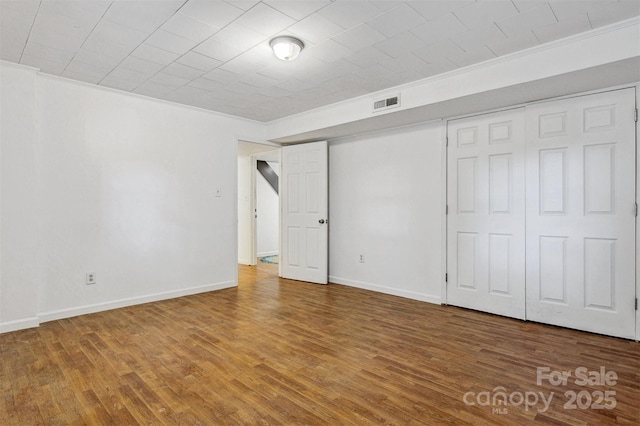 unfurnished bedroom with visible vents, ornamental molding, baseboards, and wood finished floors