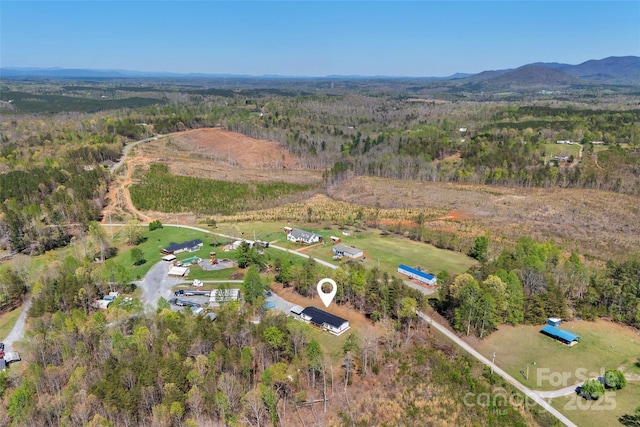 aerial view of property and surrounding area featuring a forest and a mountainous background