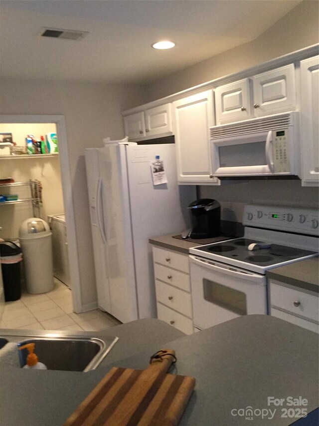 236 35th St NE, Oak Island, NC 28465 - kitchen featuring light tile patterned floors, white appliances, visible vents, white cabinetry, and dark countertops