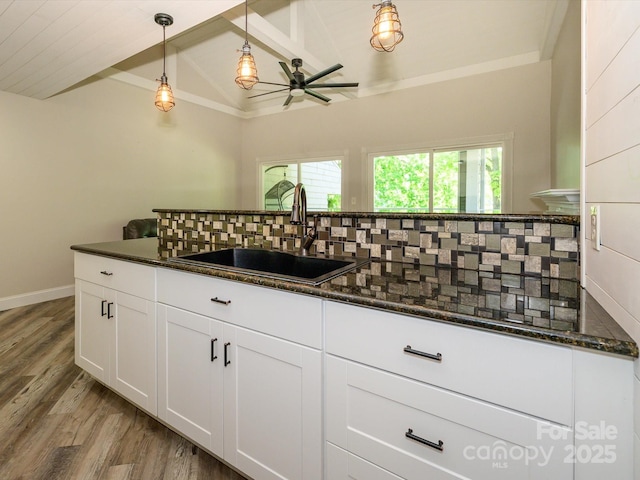 kitchen with a ceiling fan, wood finished floors, vaulted ceiling with beams, tasteful backsplash, and a sink