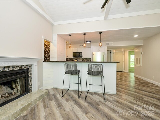 kitchen with stainless steel refrigerator, light wood finished floors, black microwave, and dark countertops