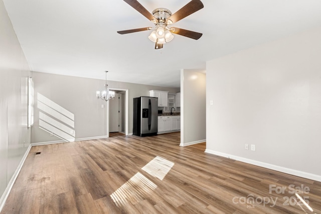 unfurnished living room with baseboards, light wood-style flooring, a sink, and ceiling fan with notable chandelier