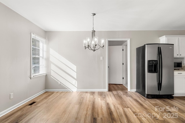 unfurnished dining area featuring light wood finished floors, a notable chandelier, baseboards, and visible vents