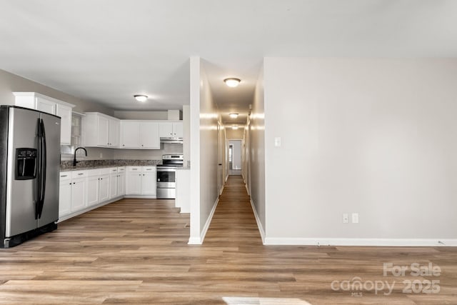 kitchen with a sink, stainless steel appliances, light wood-type flooring, under cabinet range hood, and baseboards