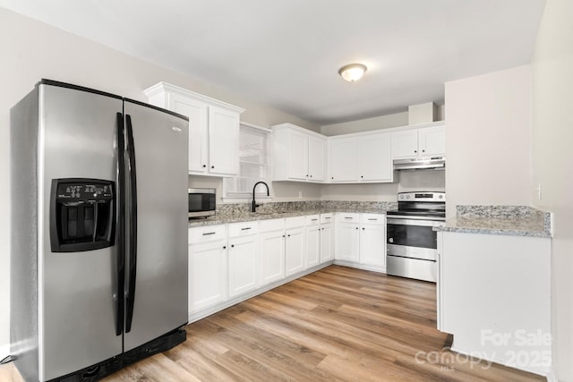 kitchen featuring a sink, stainless steel appliances, light stone counters, under cabinet range hood, and white cabinets