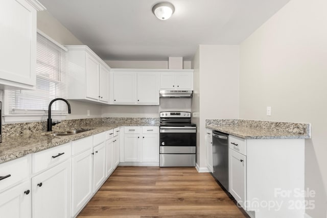 kitchen featuring under cabinet range hood, light wood finished floors, a sink, white cabinets, and appliances with stainless steel finishes