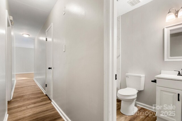 bathroom with toilet, wood finished floors, vanity, visible vents, and baseboards