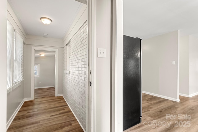 hall featuring wood finished floors, baseboards, and brick wall