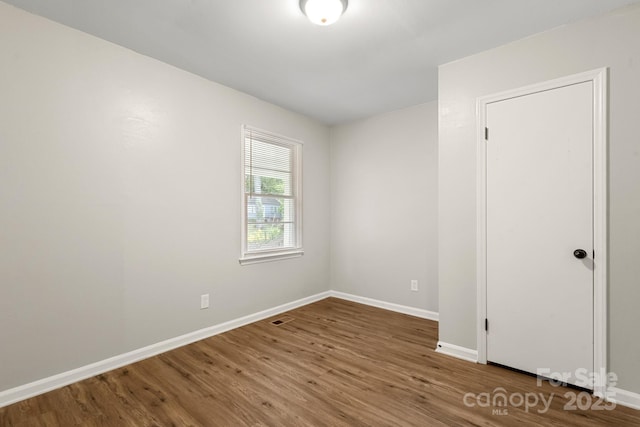 empty room featuring visible vents, wood finished floors, and baseboards