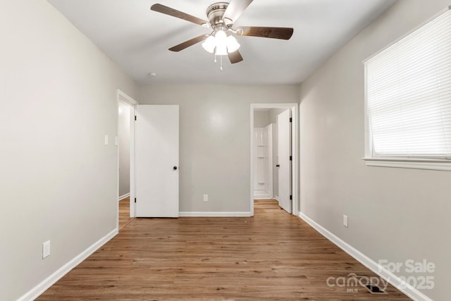 unfurnished bedroom with a ceiling fan, ensuite bath, wood finished floors, and baseboards