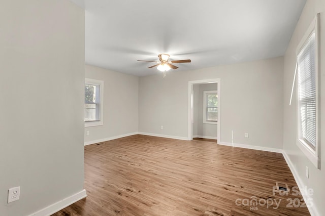 unfurnished room with baseboards, wood finished floors, a ceiling fan, and a healthy amount of sunlight