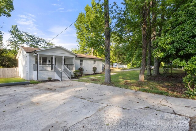 bungalow-style home with covered porch, brick siding, fence, and a front lawn