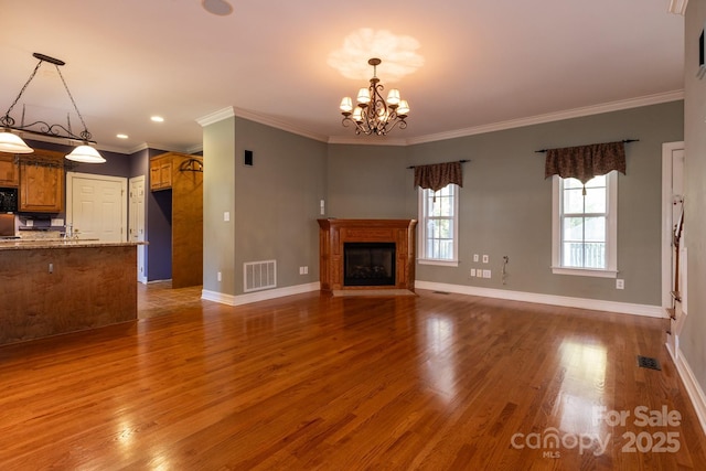 unfurnished living room with crown molding, wood finished floors, baseboards, a fireplace with raised hearth, and a chandelier