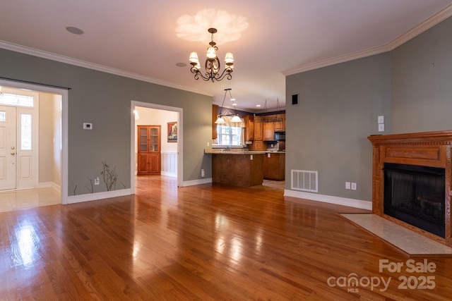 unfurnished living room with visible vents, wood finished floors, baseboards, a notable chandelier, and ornamental molding