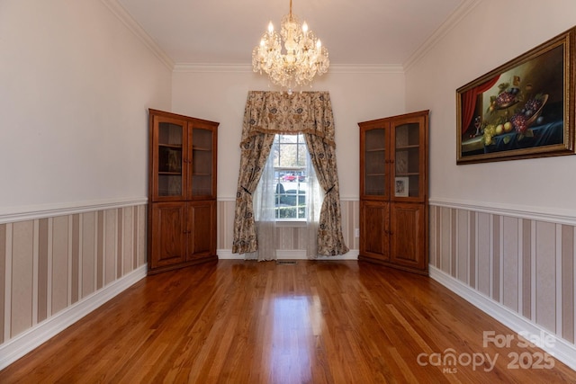 unfurnished dining area featuring crown molding, wainscoting, wood finished floors, and a chandelier