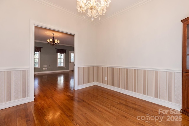 unfurnished room with crown molding, baseboards, wood finished floors, and a chandelier