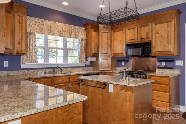 kitchen with brown cabinets, black microwave, light stone counters, a sink, and an island with sink