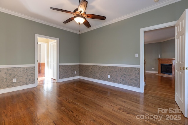spare room with ceiling fan, crown molding, a fireplace, dark wood-style floors, and wallpapered walls
