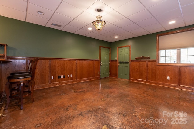 unfurnished room featuring wooden walls, wainscoting, finished concrete floors, and visible vents