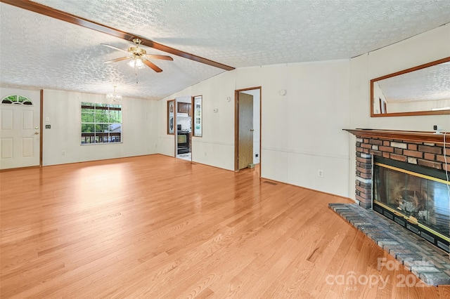 unfurnished living room with a fireplace, a textured ceiling, ceiling fan with notable chandelier, wood finished floors, and vaulted ceiling