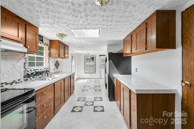kitchen featuring a sink, freestanding refrigerator, black range with electric cooktop, under cabinet range hood, and a skylight