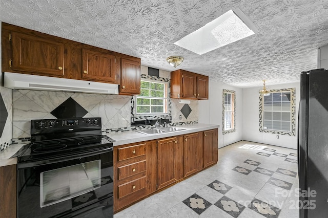 kitchen with a skylight, light countertops, a sink, black appliances, and under cabinet range hood