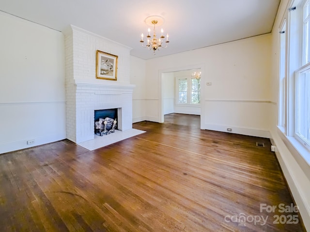 unfurnished living room with a chandelier, wood finished floors, a fireplace, and baseboards