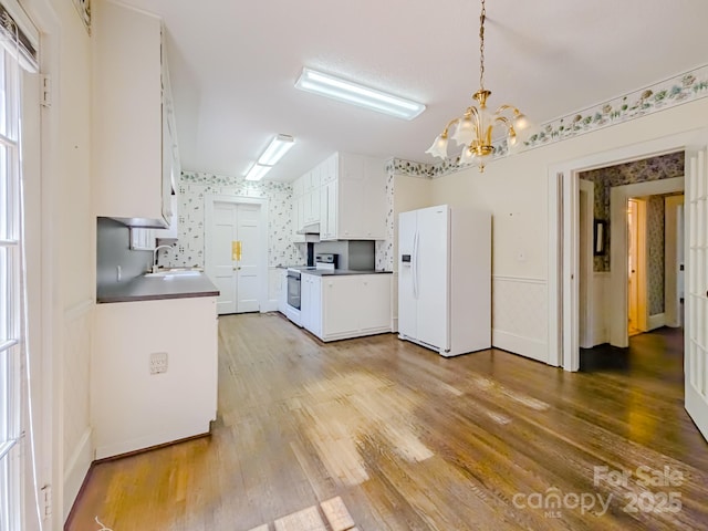 kitchen with white appliances, a sink, a chandelier, light wood-style flooring, and white cabinets