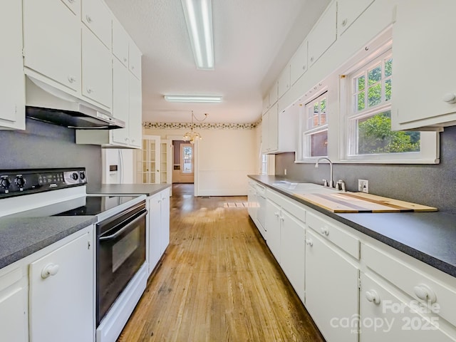 kitchen featuring white appliances, under cabinet range hood, white cabinetry, light wood-style floors, and dark countertops