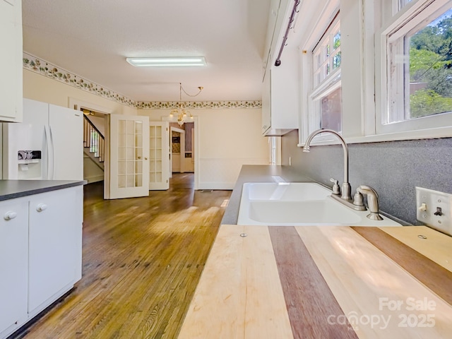 kitchen featuring white refrigerator with ice dispenser, a sink, wood finished floors, a chandelier, and white cabinets