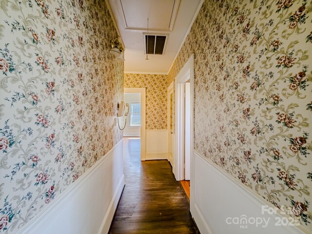 corridor with attic access, wallpapered walls, wainscoting, dark wood-type flooring, and ornamental molding