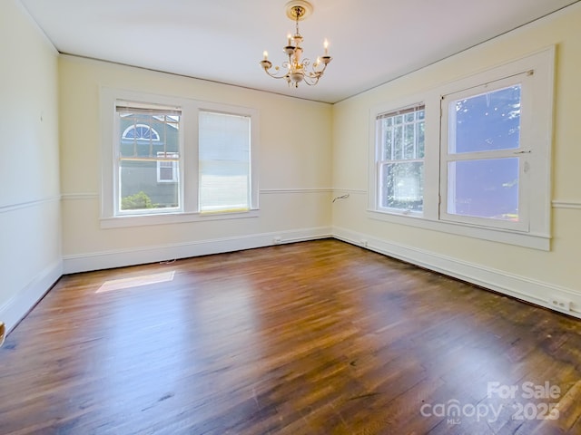spare room featuring a chandelier, wood finished floors, and baseboards