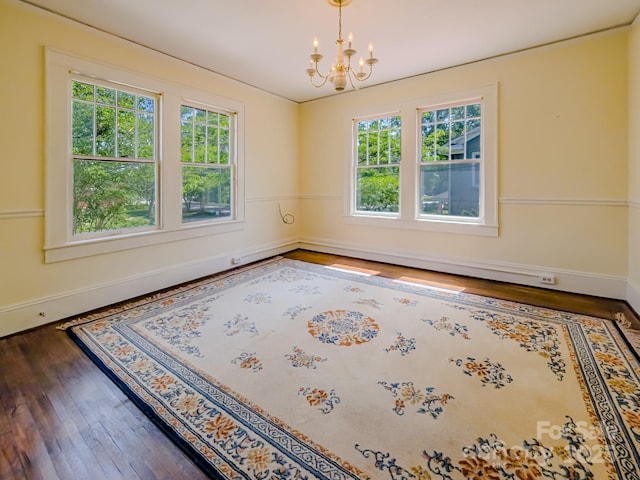 spare room featuring plenty of natural light, hardwood / wood-style flooring, a chandelier, and baseboards