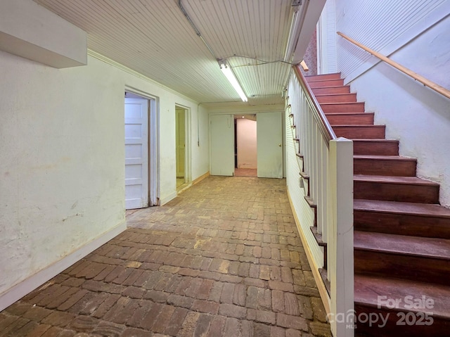 hallway featuring brick floors, stairway, and baseboards