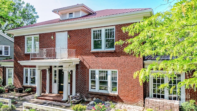 view of front facade with a balcony, brick siding, and metal roof