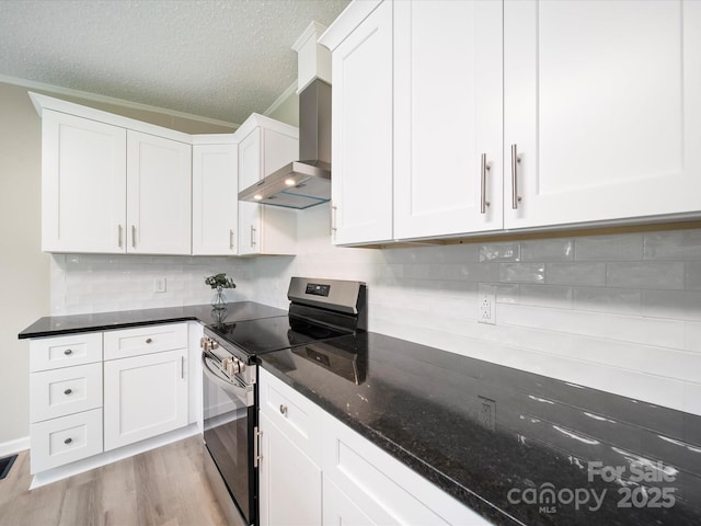 kitchen with stainless steel range with electric cooktop, wall chimney exhaust hood, light wood-type flooring, dark stone countertops, and white cabinets