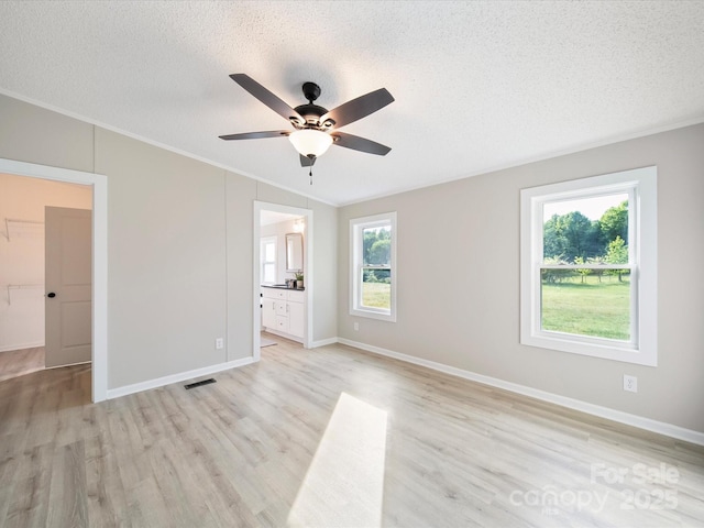 unfurnished bedroom featuring ornamental molding, a textured ceiling, light wood-style floors, baseboards, and connected bathroom