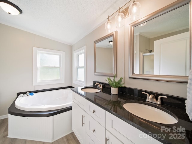 bathroom featuring a textured ceiling, wood finished floors, vaulted ceiling, a bath, and double vanity