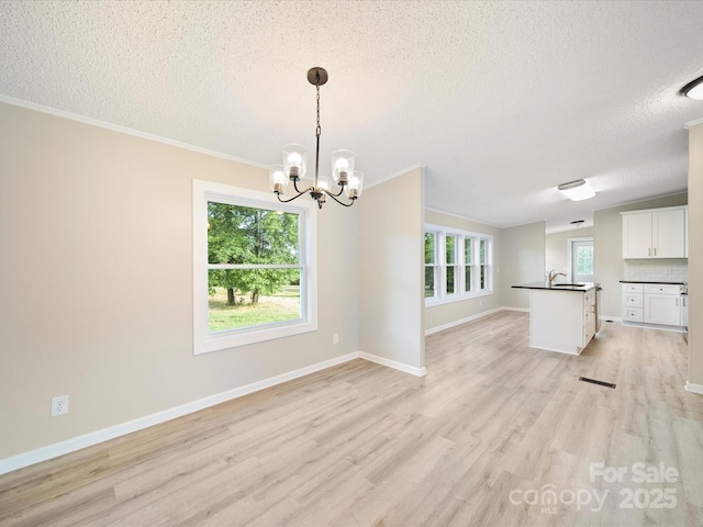 unfurnished dining area featuring a textured ceiling, a chandelier, light wood-style floors, ornamental molding, and baseboards