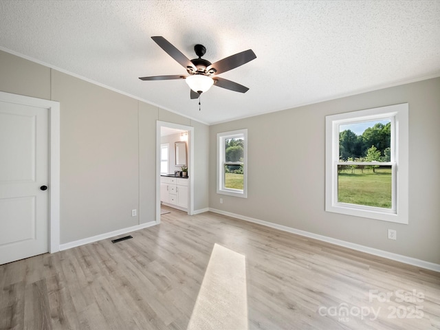 unfurnished bedroom featuring crown molding, light wood-style flooring, a textured ceiling, baseboards, and ensuite bathroom