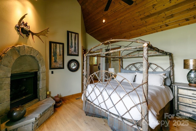 bedroom featuring lofted ceiling, wood finished floors, wood ceiling, baseboards, and a stone fireplace