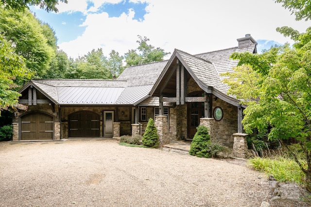 view of front of home featuring stone siding, driveway, a chimney, and a garage