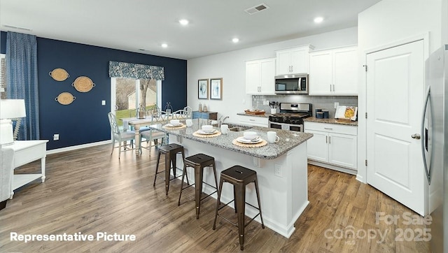 kitchen featuring appliances with stainless steel finishes, a sink, a breakfast bar, light stone counters, and white cabinetry