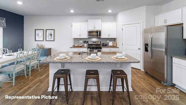 kitchen featuring stainless steel appliances, a kitchen bar, dark wood finished floors, white cabinetry, and recessed lighting